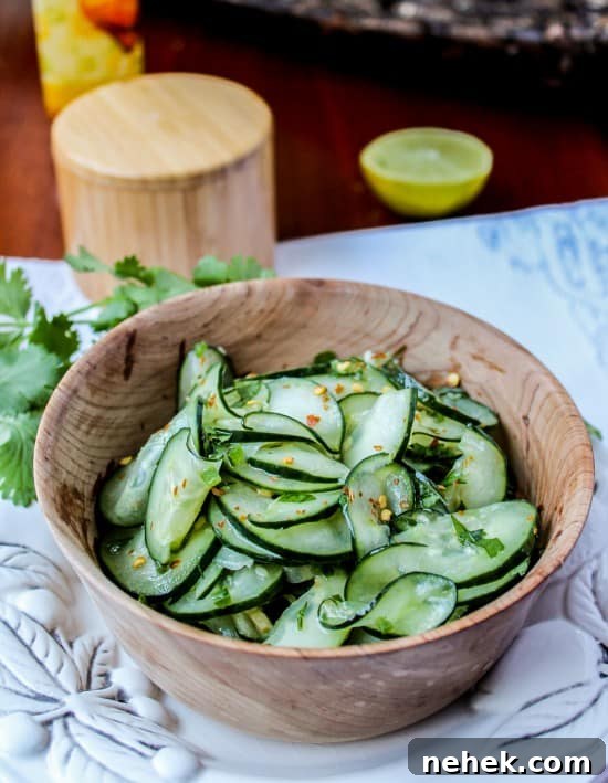 Cilantro Lime Cucumber Salad Mexican cucumber salad with cilantro and lime in a wooden salad bowl on a white platter with cilantro and lime in background.
