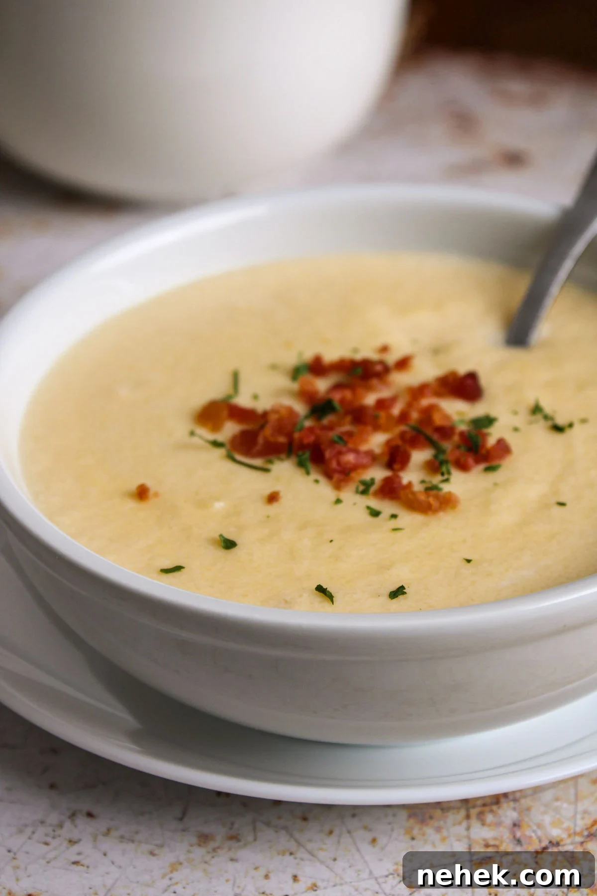 Bowl with cheesy cauliflower soup garnished with bacon bits and chives.