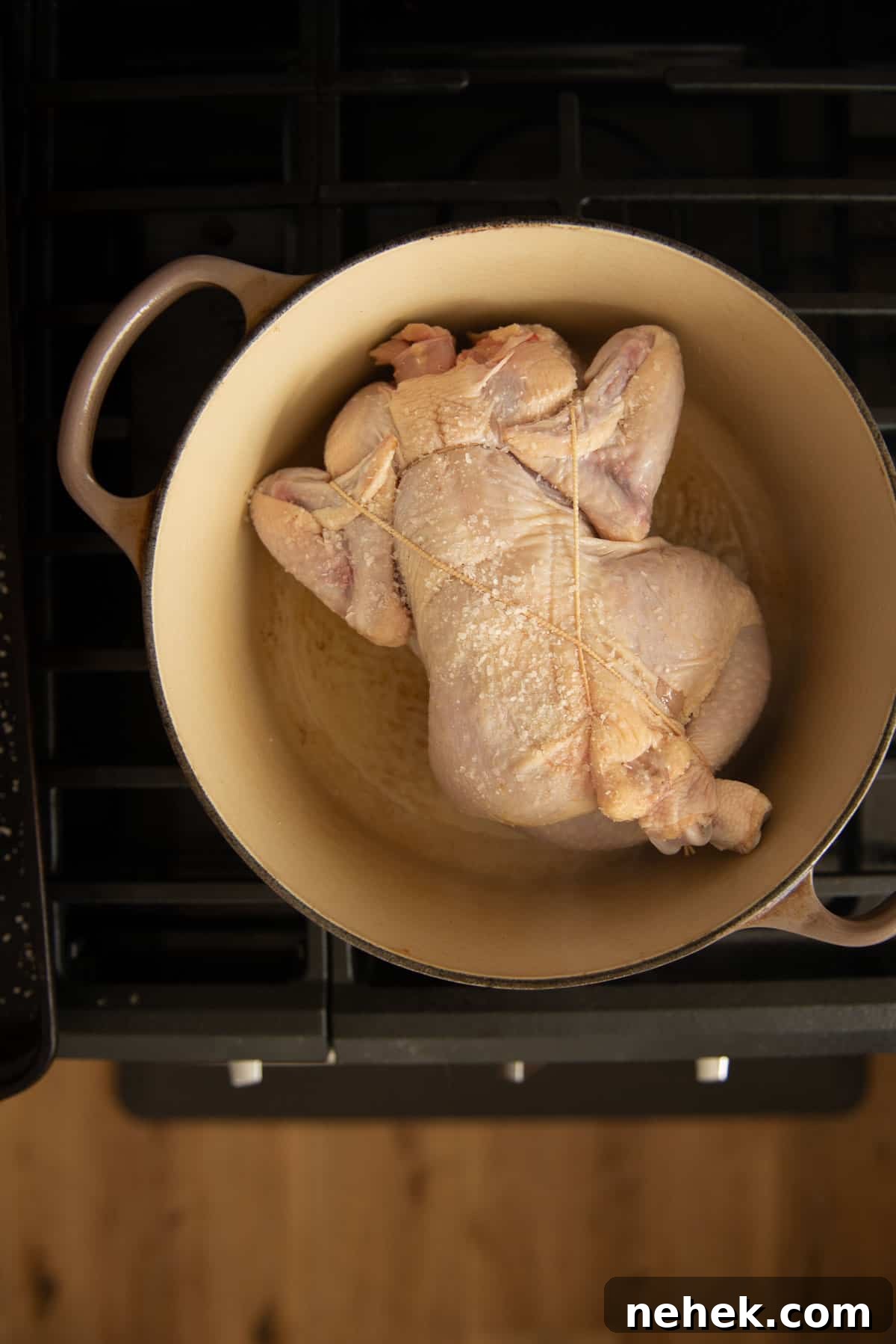 A chicken is searing, breast side down, in a Dutch oven on top of a stove.