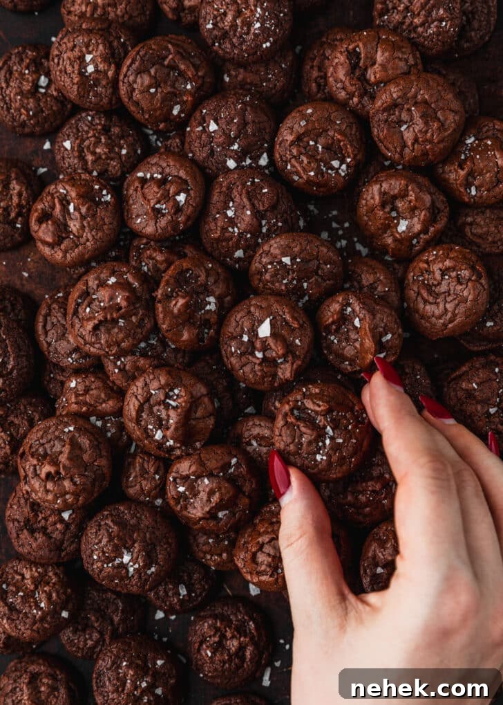 A hand grabbing a cookie from a tray of mini chocolate brownie crinkle cookies.