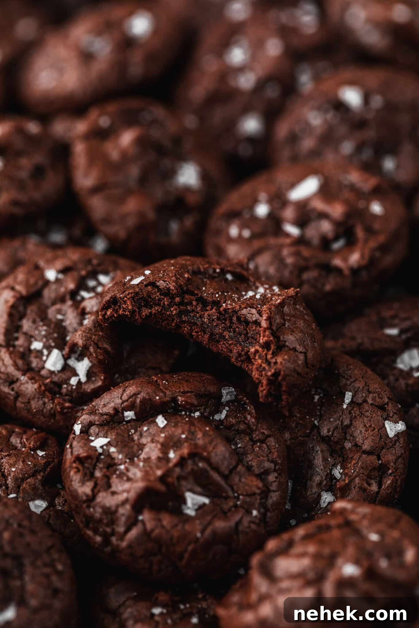 A cookie with a bite taken out of it on piles of chocolate mini brownie crinkle cookies.