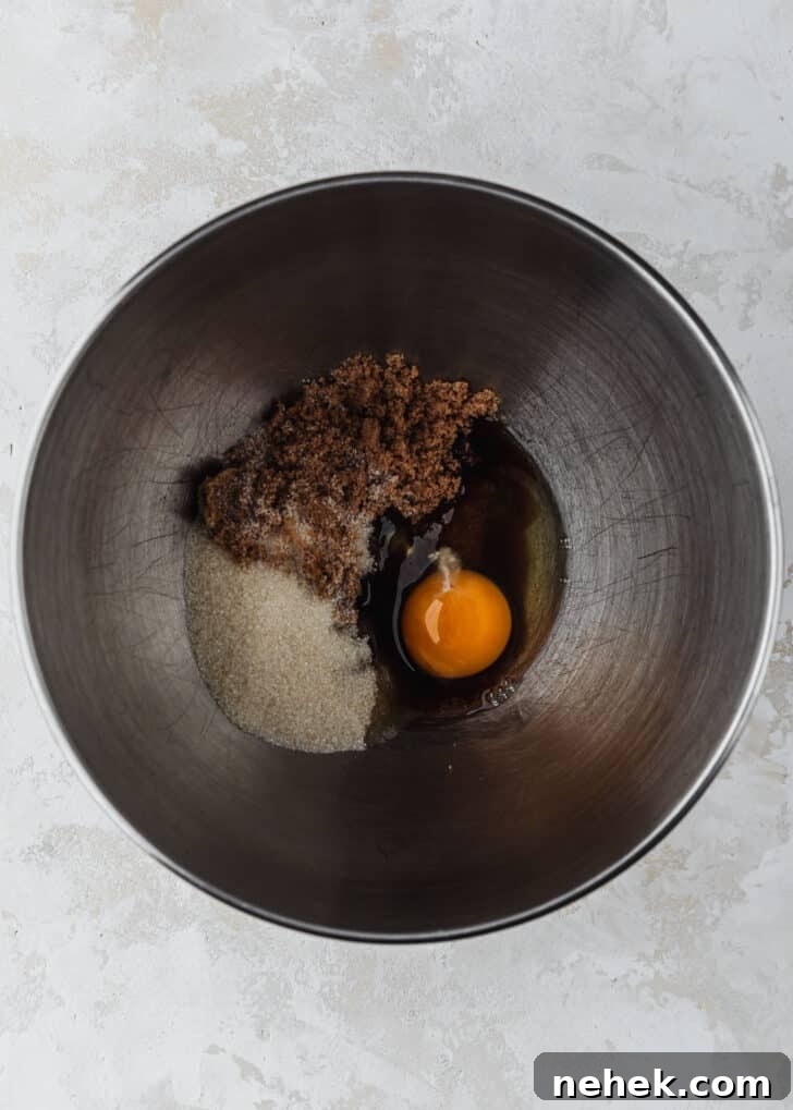 A silver bowl of brown sugar, white sugar, and an egg on a tan table.