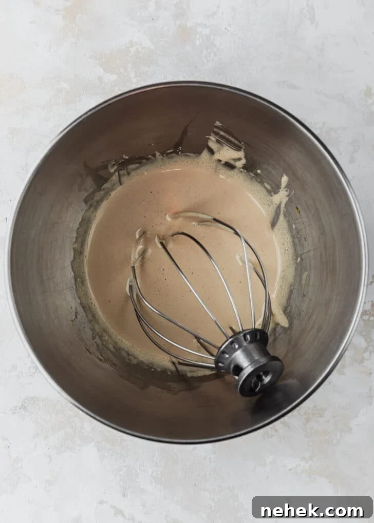 A silver bowl of whipped sugar and eggs on a tan counter.