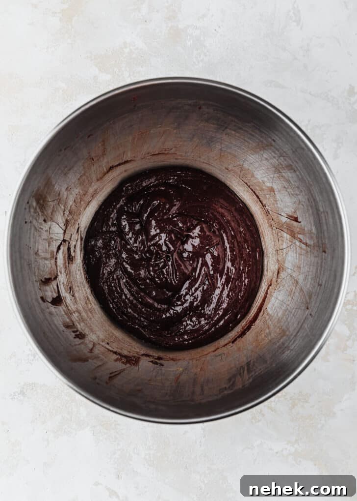 A silver bowl of whipped sugar, eggs, and chocolate on a tan counter.