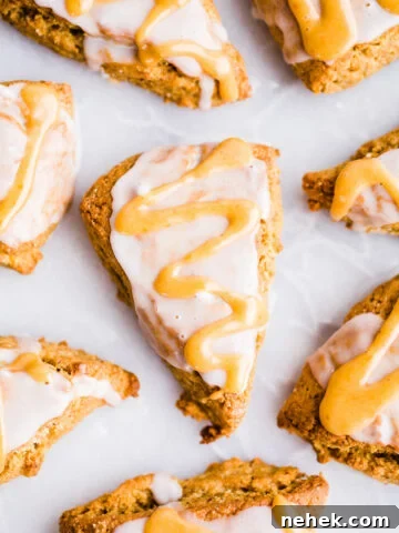 Pumpkin scones with vanilla and pumpkin glaze on white parchment paper.