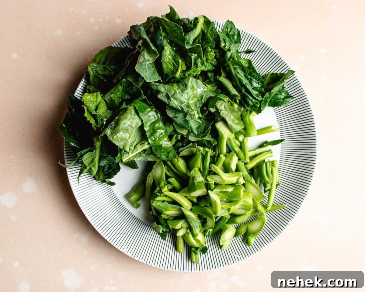 A white plate with a black striped rim holds chopped Chinese broccoli leafy greens arranged stems separately from leafy parts on a light beige surface, similar to toppings served with beef with Chinese broccoli.
