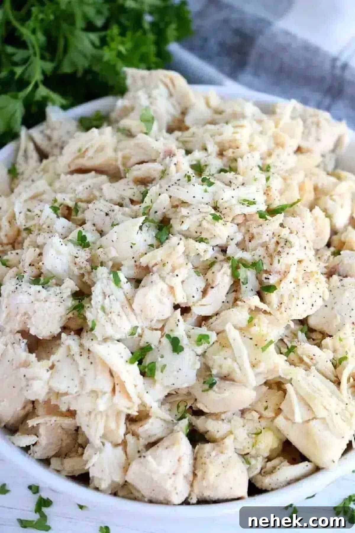 A bowl of shredded cooked chicken, garnished with chopped parsley and black pepper—perfect for anyone learning how to make shredded chicken on the stove.