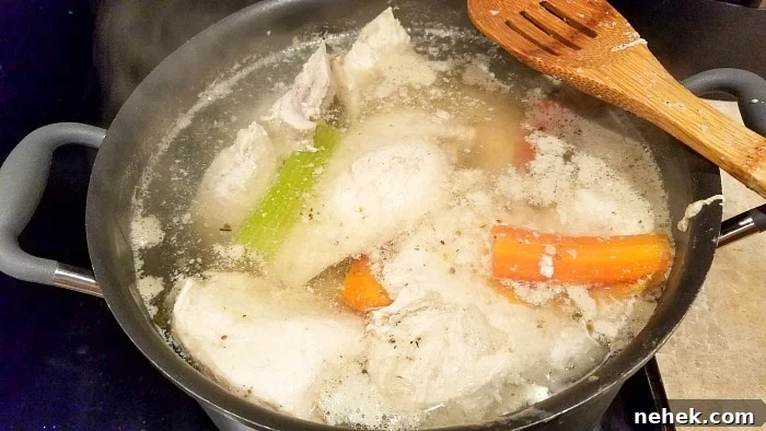 A pot of boiling water with chicken pieces, carrots, and celery simmers on the stove—perfect for learning how to make shredded chicken. A wooden spatula rests on the edge, as steam rises from the bubbling broth.