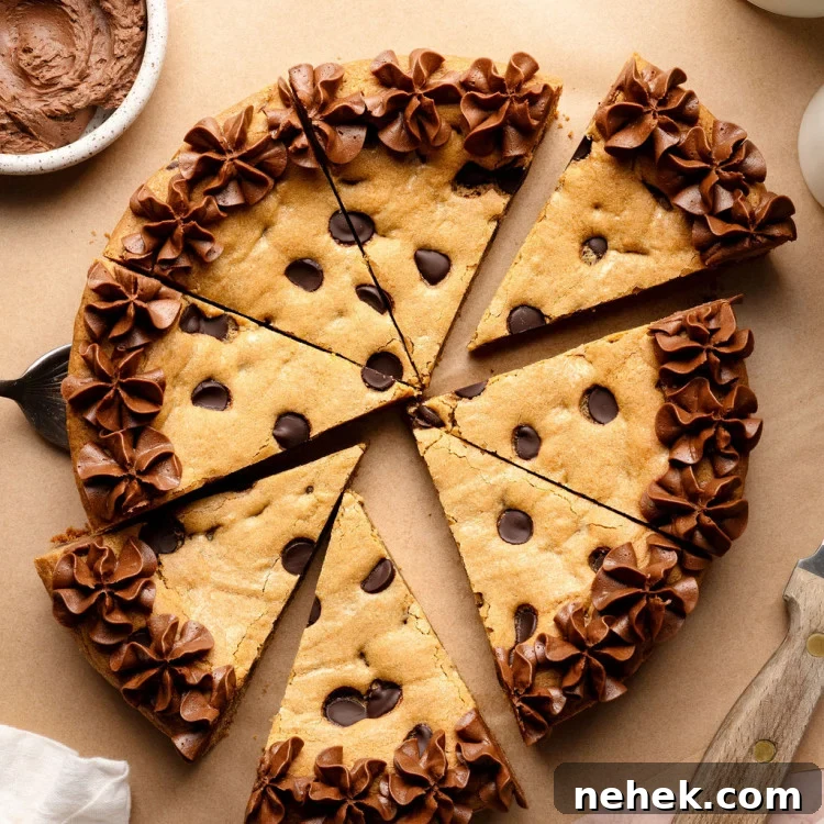 A sliced chocolate chip cookie cake decorated with piped chocolate frosting