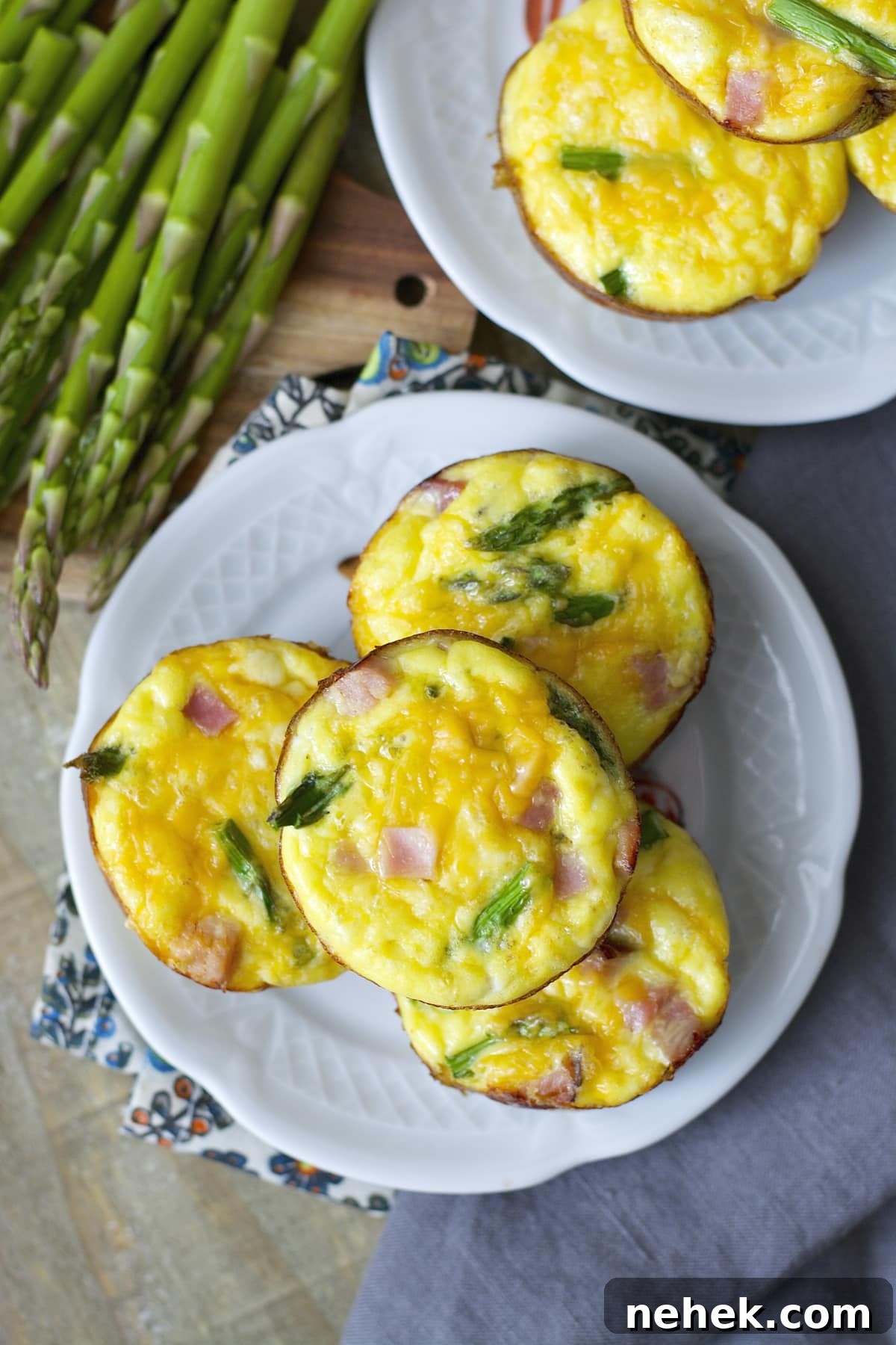 Overhead view of two plates piled with mini ham asparagus quiche, next to a bunch of fresh asparagus. 