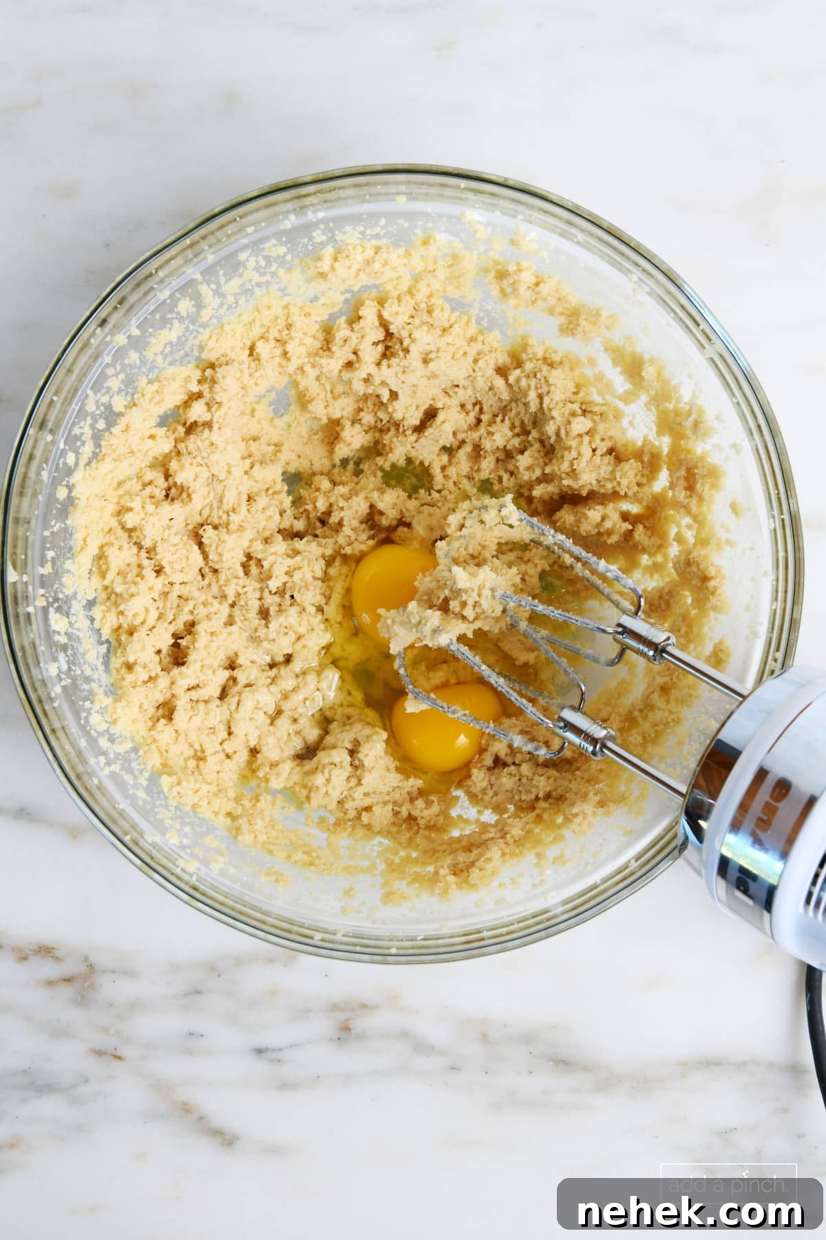 Eggs are beaten into the butter mixture with a hand mixer for Oatmeal Raisin Cookies.