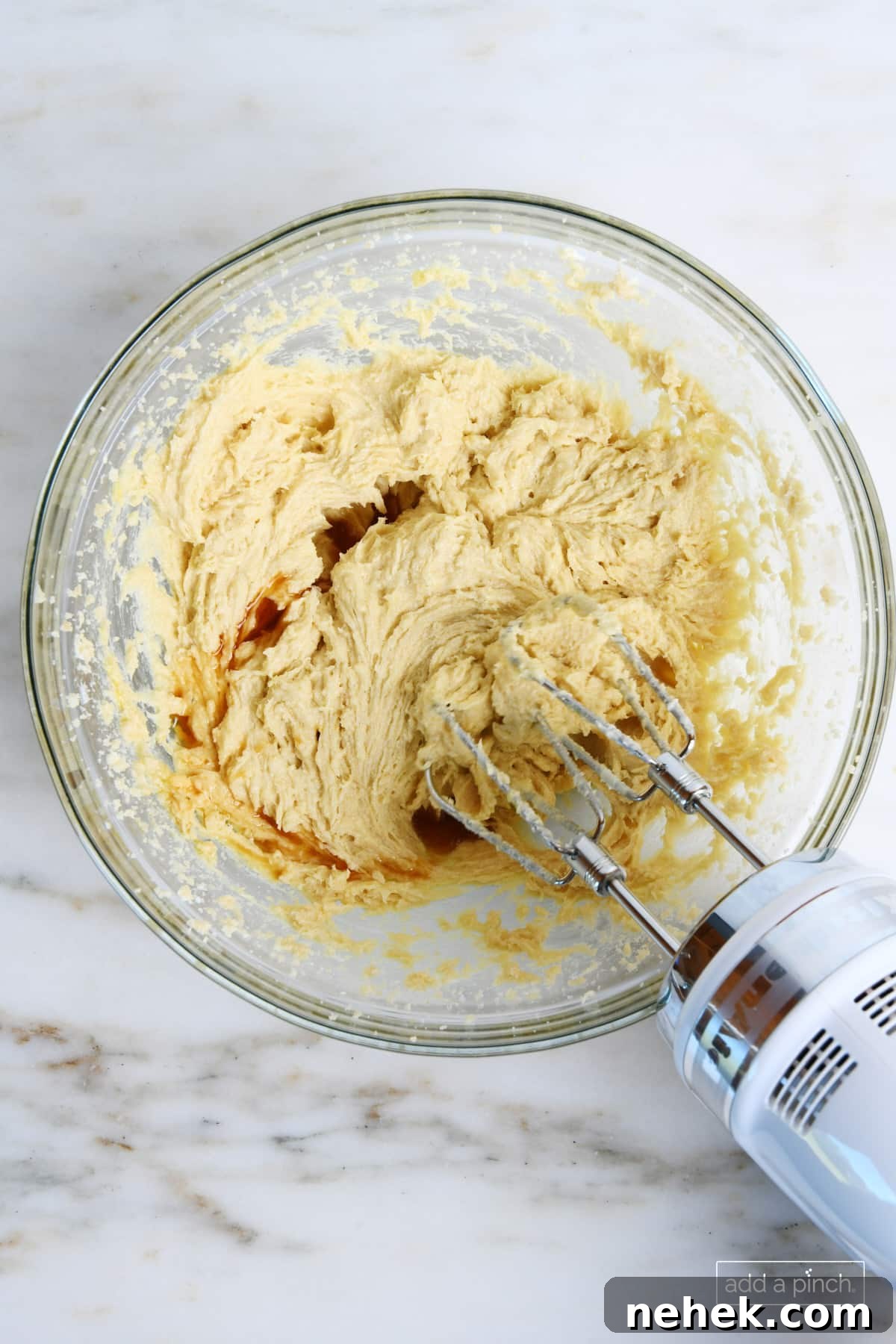 Vanilla extract is mixed into wet ingredients for cookie dough with a hand mixer.