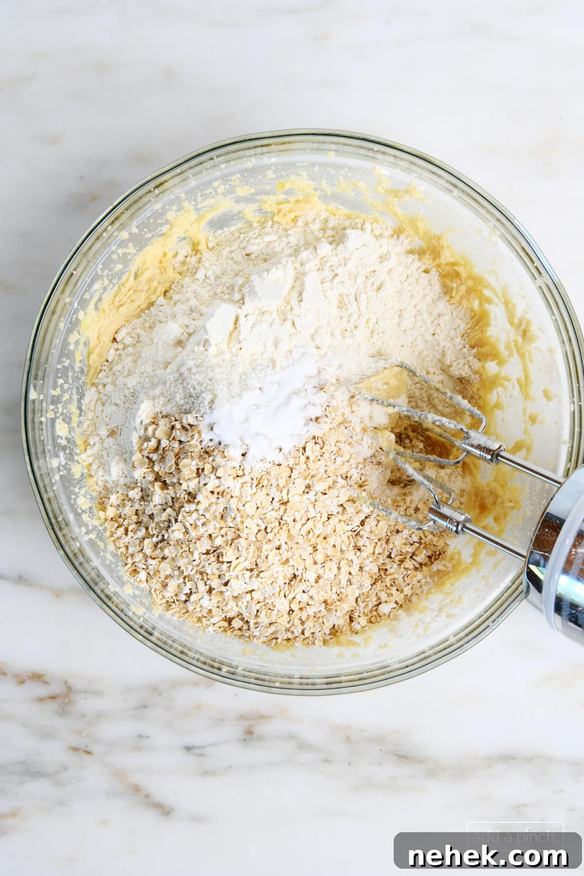 Dry ingredients of flour, baking soda, salt and quick oats are added to glass bowl with wet ingredients and mixed with a hand mixer. 