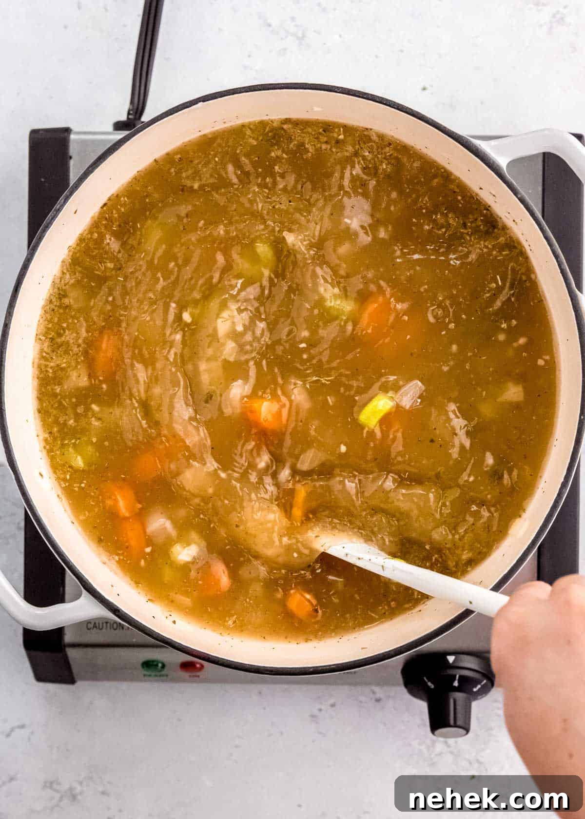 Classic Homemade Chicken Noodle Soup Recipe for Comforting Meals 7 a large spoon stirring a pot full of simple veggies and seasonings in broth