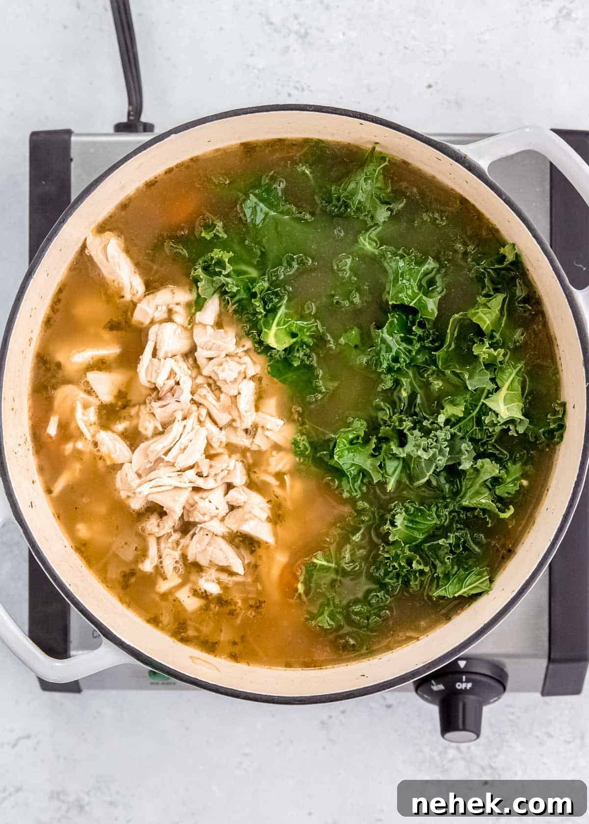 Classic Homemade Chicken Noodle Soup Recipe for Comforting Meals 8 shredded chicken and chopped kale added into a large pot filled with broth, egg noodles, and vegetables