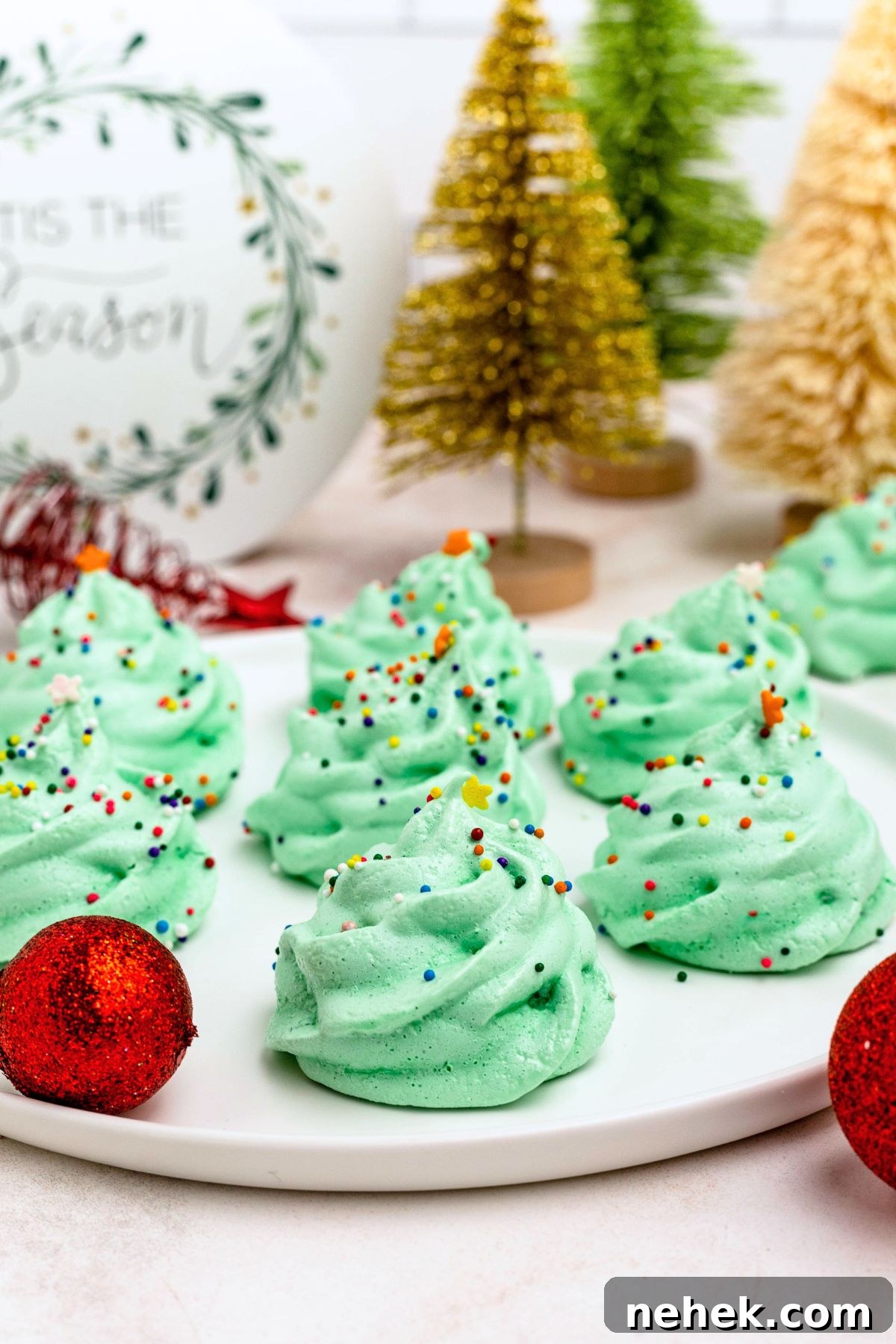 Meringue Christmas Tree Cookies: Festive Dessert Recipe Ideas 2 Green meringue trees on a white plate, with Christmas ornaments and mini trees on the table.