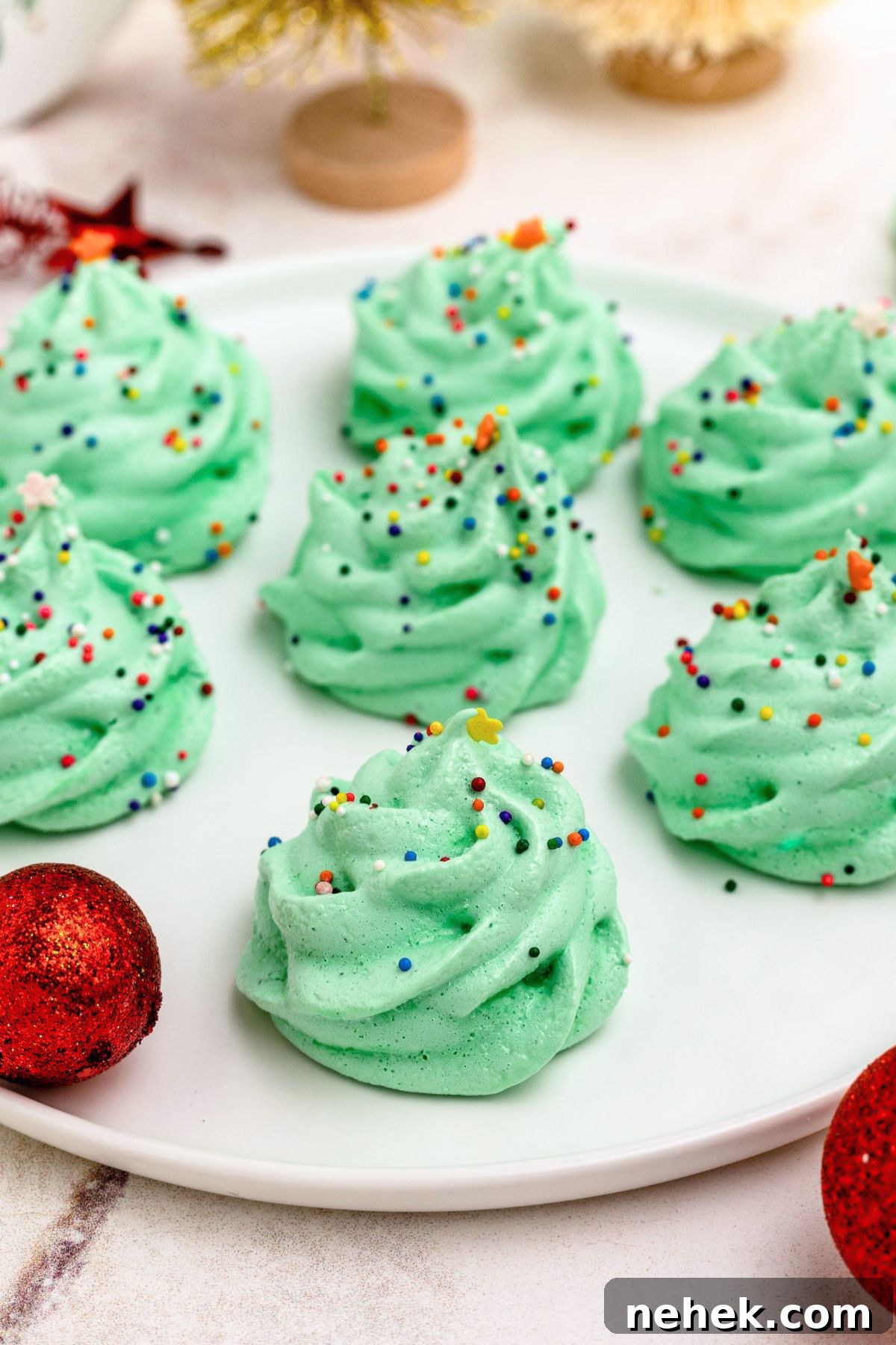 Meringue Christmas Tree Cookies: Festive Dessert Recipe Ideas 7 Green meringue trees on a white plate, with ornaments around the plate.
