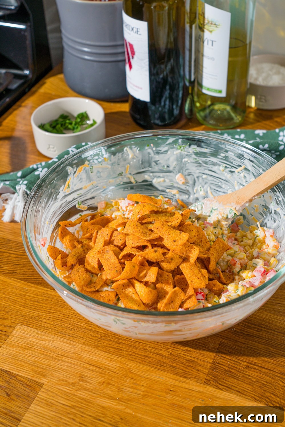 Spicy Corn Salad with Chili Cheese Fritos Crunch 9 A glass bowl with a corn and pepper mixture tossed in sour cream dressing with chili cheese fritos on top. The bowl is on a wooden counter.