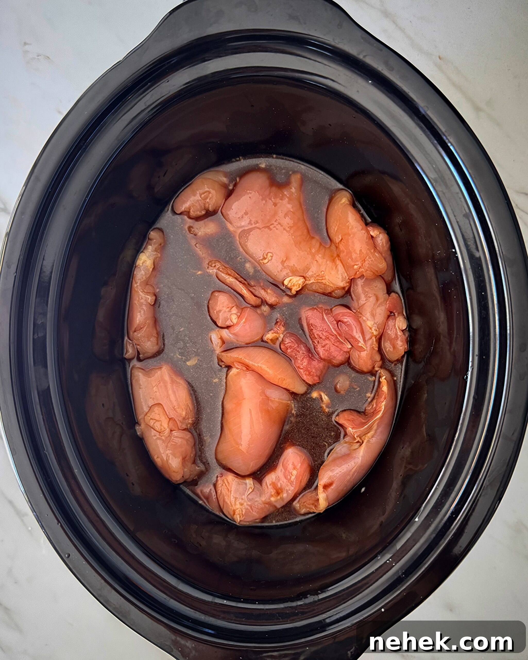 overhead shot of uncooked teriyaki chicken in a black slow cooker