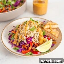 Bowl of colorful salad with brown rice, peanut sauce, tofu and veggies. Jar of sauce in background.