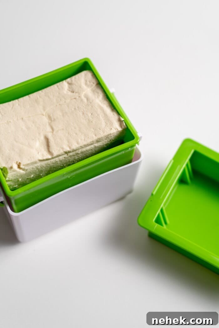 A block of tofu in a rectangular box tofu press.
