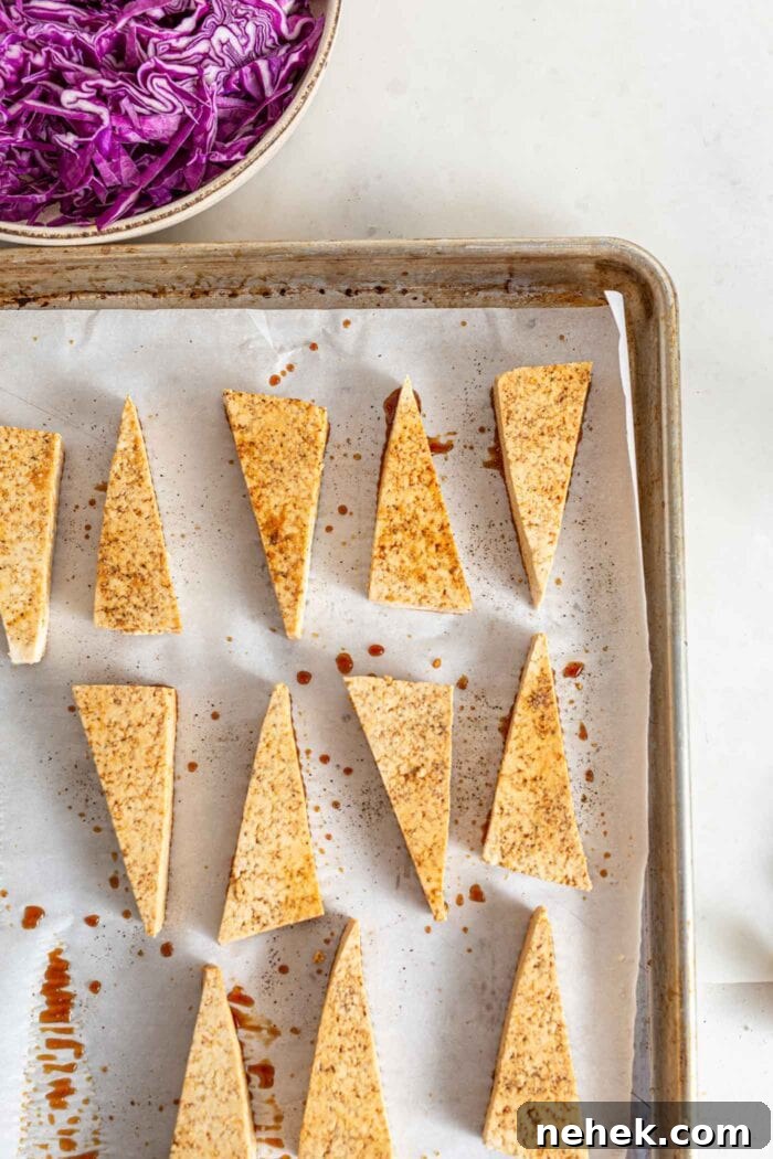 Sliced triangles of tofu with sauce on them on a baking pan.