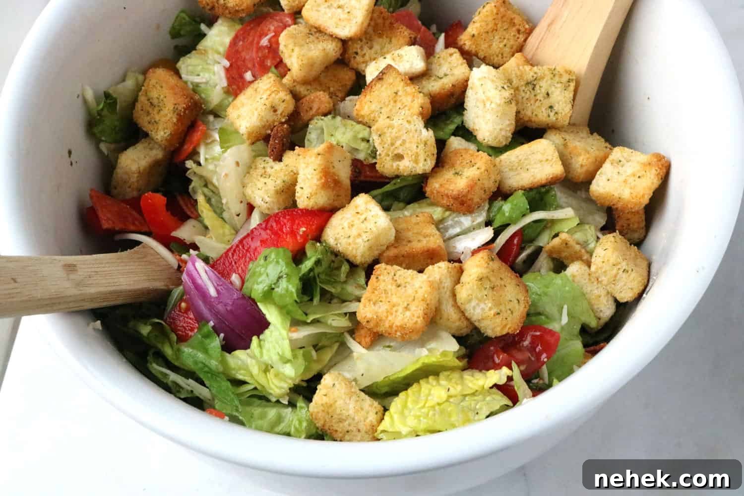 Classic Italian Salad with Homemade Dressing Recipe 6 close-up of Italian salad topped with croutons in a white bowl with salad forks.