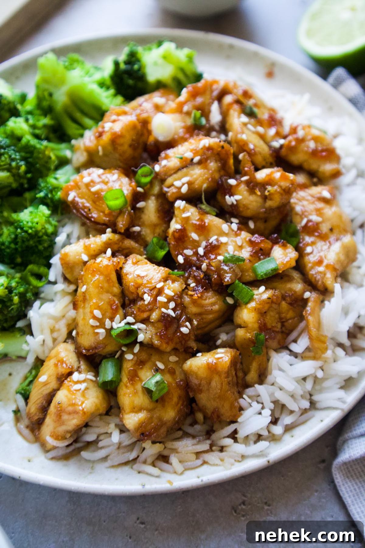 white plate with chicken over top of white rice and a side of broccoli topped with sesame seeds and green onion.