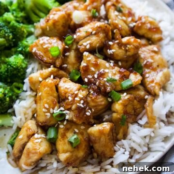 white plate with chicken over top of white rice and a side of broccoli topped with sesame seeds and green onion.