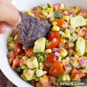 grilled corn avocado salsa in a white bowl with a tortilla chip dipping into it