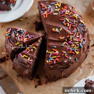 Quick Single-Layer Chocolate Cake Recipe for Perfect Moistness 13 Angled image of sliced single layer chocolate cake on parchment paper with slices of cake on small dessert plates around it and a knife on parchment paper.