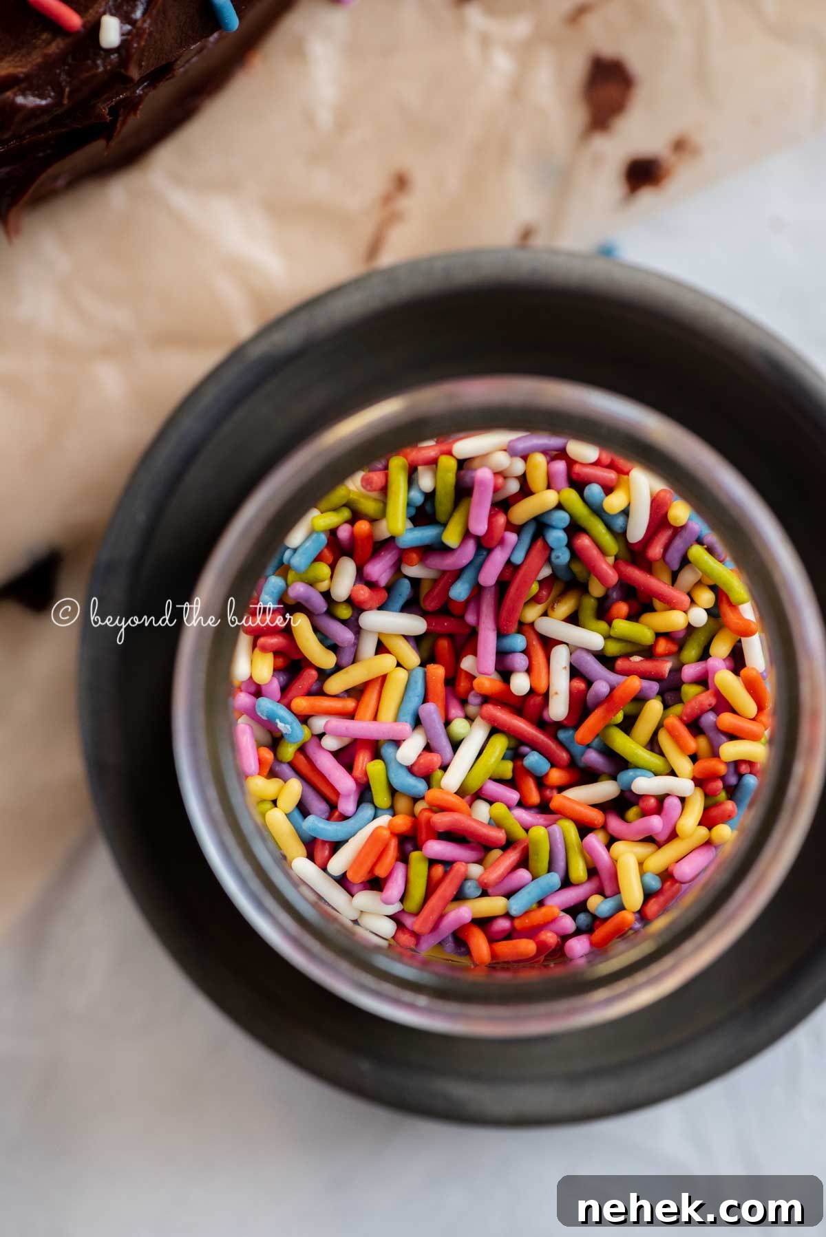 Quick Single-Layer Chocolate Cake Recipe for Perfect Moistness 5 Small bowl of rainbow sprinkles on a dark plate with chocolate cake next to it | All Images © Beyond the Butter®