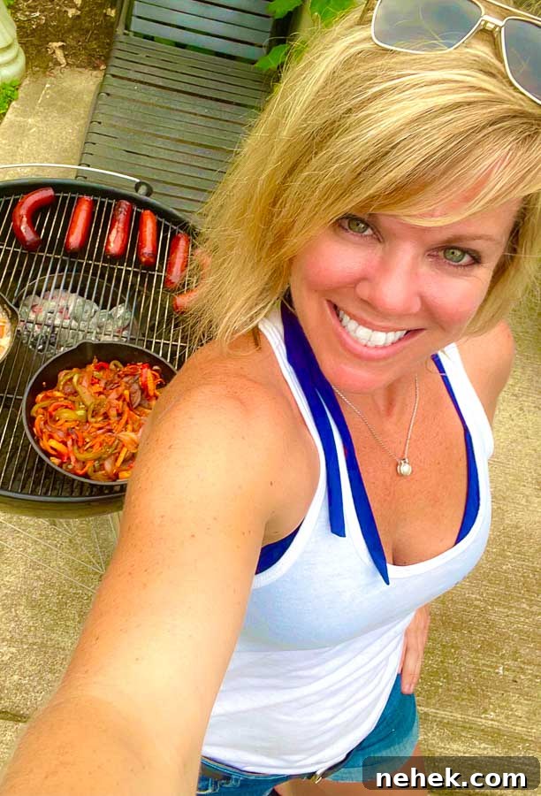 Jennifer with weber grill behind grilling sausages, onions, and peppers