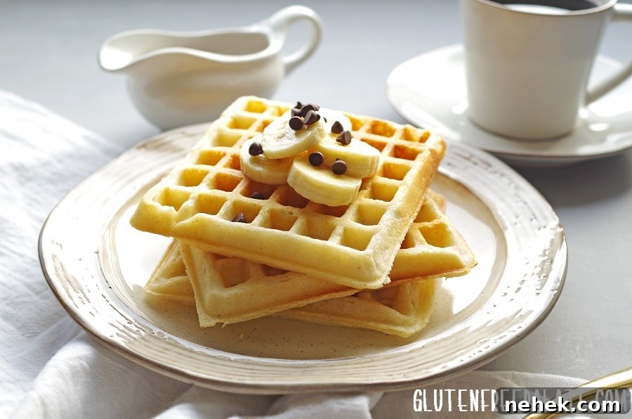 Three gluten-free waffles stacked on a plate topped with sliced banana and chocolate chips, next to a cup of coffee.