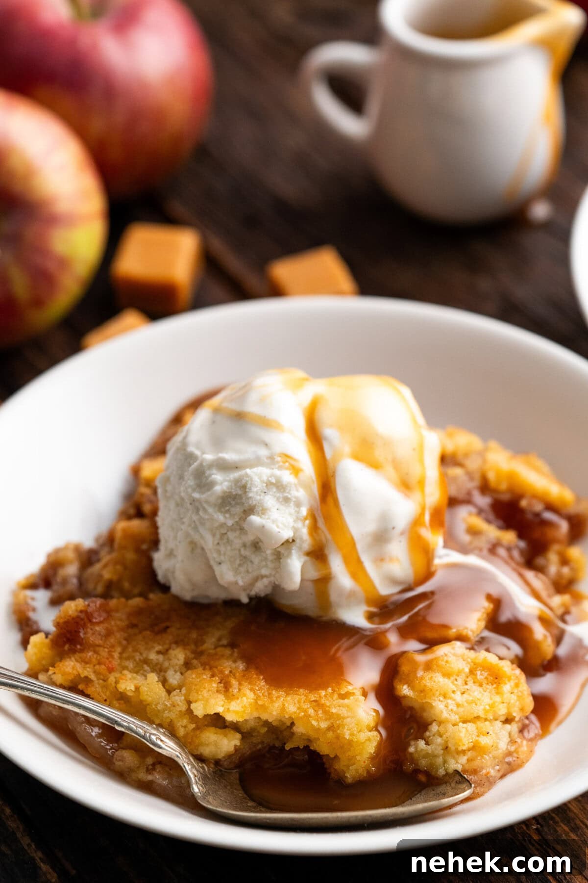 Caramel Apple Dump Cake in a bowl topped with ice cream and caramel sauce