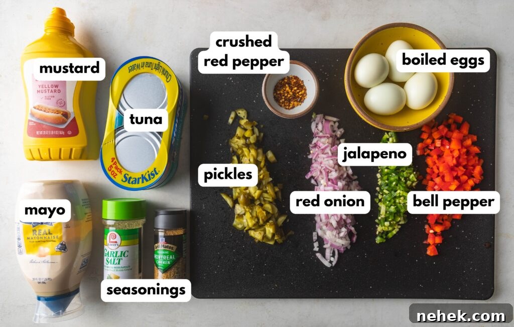 Spicy Tuna Salad recipe ingredients  on a black cutting board and white background. Mustard, Tuna, Mayonnaise, Seasonings, Crushed Red Pepper, Diced Pickles, Diced Red Onion, Diced Jalapeño, Diced Red Bell Pepper, and 4 boiled eggs