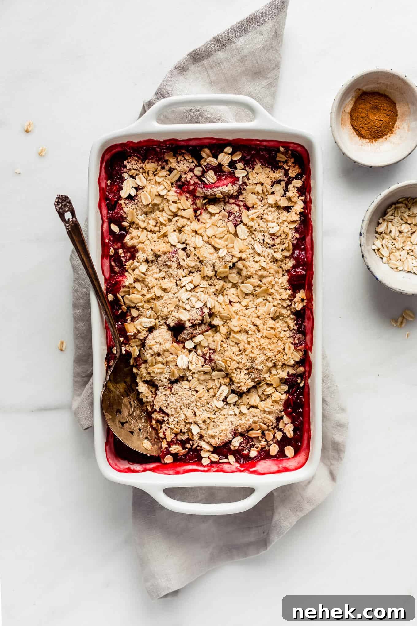 strawberry rhubarb crisp in a baking dish with a serving spoon.