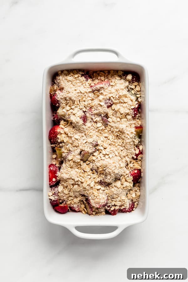 a white baking dish with strawberries and rhubarb in it topped with an oat crumble topping