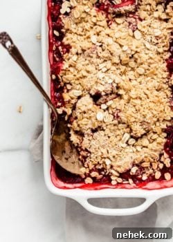 strawberry rhubarb crisp in a baking dish with a spoon in it