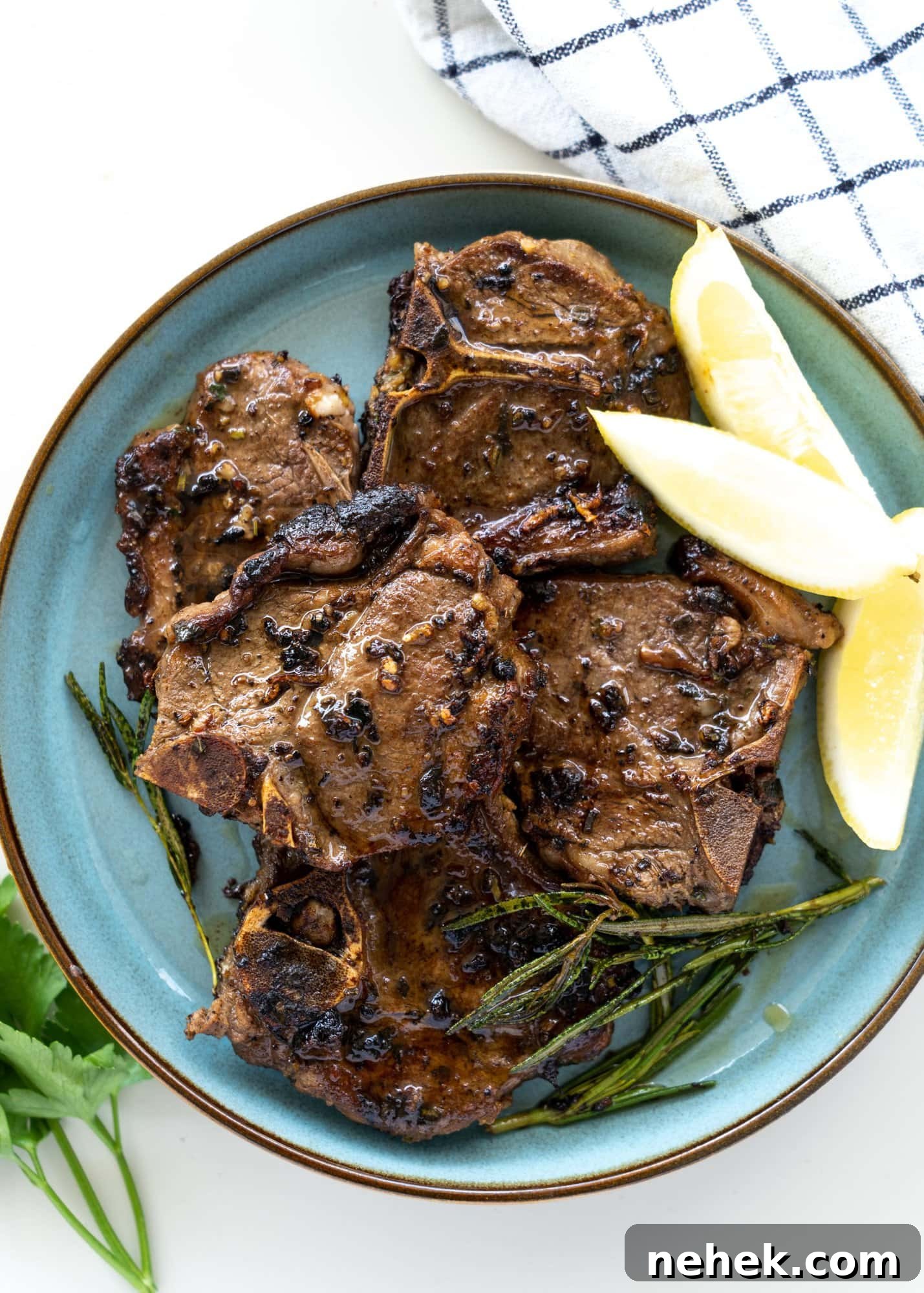 Crispy Pan-Seared Lamb Chops with Garlic Herb Butter 5 Mediterranean lamb chops seared and served on a blue plate with some lemon slices and parsley.