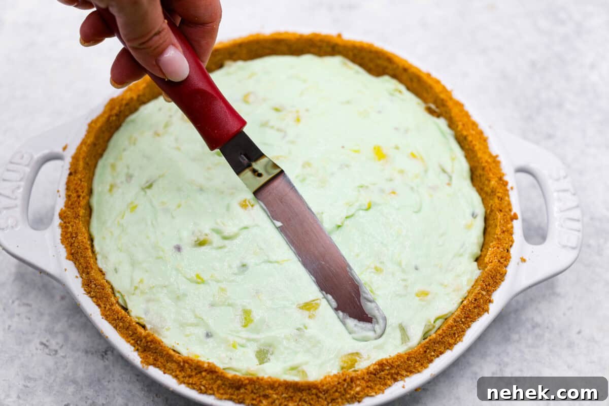Third photo of a small spatula smoothing the top of the no-bake pistachio cream pie.