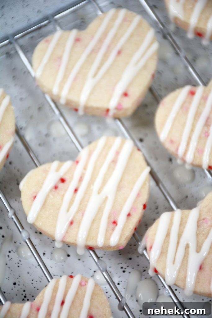 Mini Valentine Shortbread Cookies Recipe for Cute Heart Treats 5 glaze being drizzled over the top of mini heart shaped cookies on a wire rack.