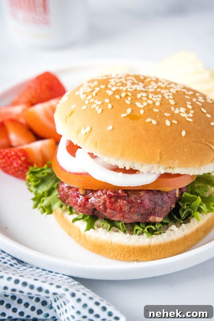 How to Make Smoked Burgers That Stay Juicy and Flavorful 3 looking down on a plate with a smoked hamburger on a bun with a plate of strawberries