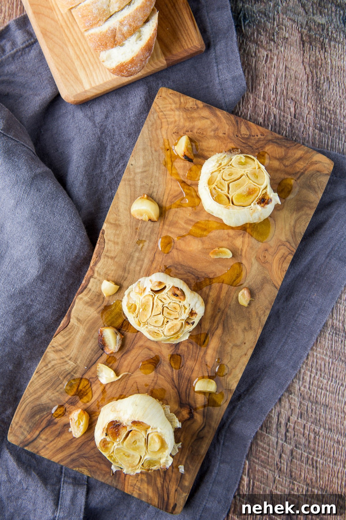 Overhead view of a wood boards one with three roasted garlic heads and one with bread