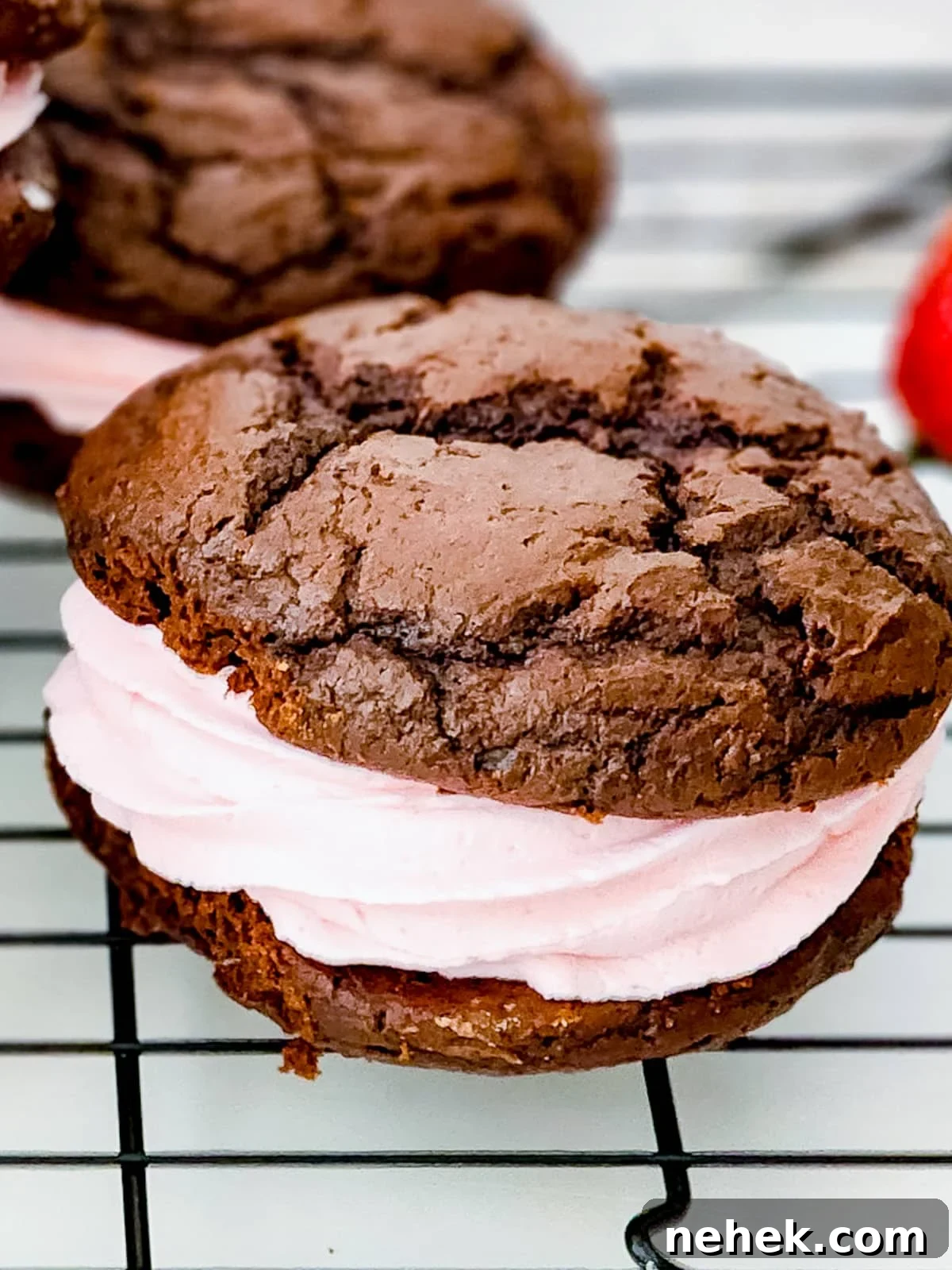 Chocolate Whoopie Pies with Strawberry Frosting Recipe 2 A chocolate whoopie pie filled with pink strawberry frosting on a cooling rack.