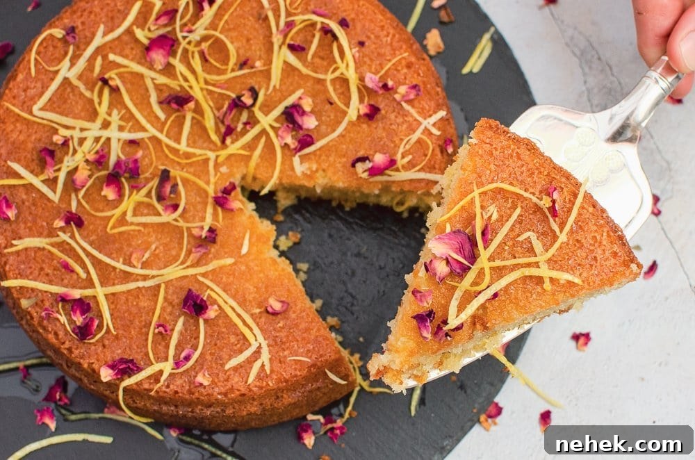 Perfect Lemon Drizzle Cake Recipe — Moist, Zesty Slice 2 Slice of flawless lemon drizzle cake decorated with lemon zest and rose petals being lifted up with a silver cake knife