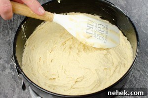 Perfect Lemon Drizzle Cake Recipe — Moist, Zesty Slice 9 Cake mixture being spread into a black round cake tin with a wooden and white spatula