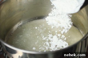 Perfect Lemon Drizzle Cake Recipe — Moist, Zesty Slice 11 Icing sugar being poured into the lemon juice in a silver cooking pot