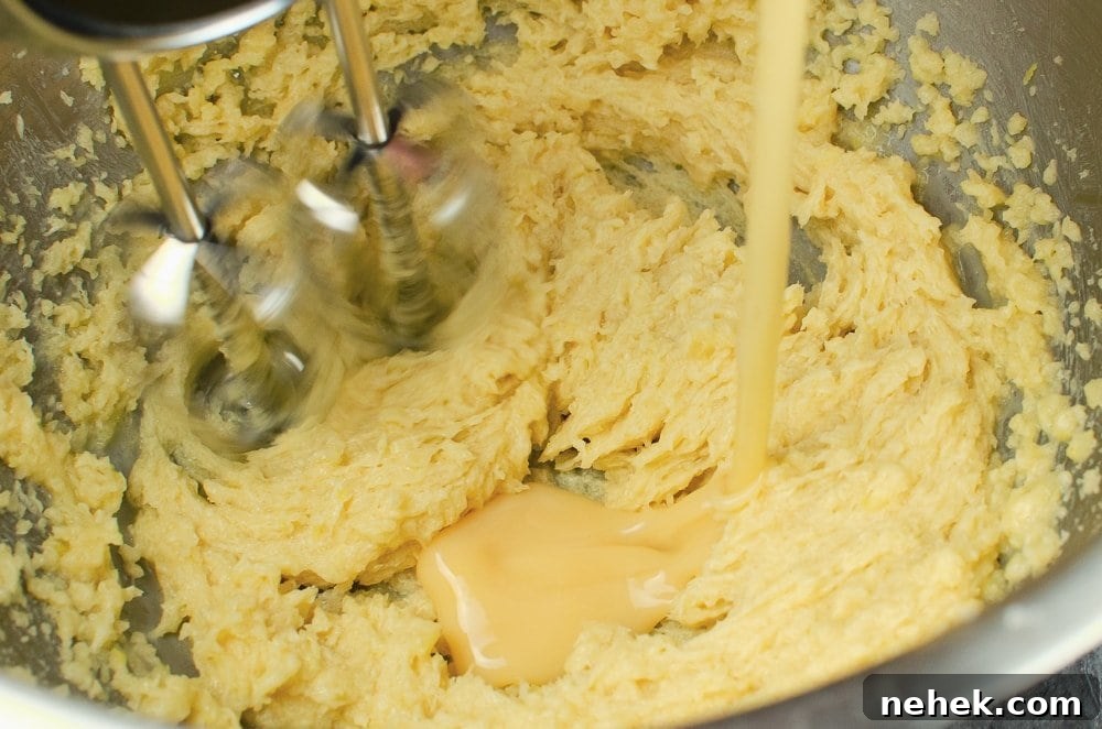 Perfect Lemon Drizzle Cake Recipe — Moist, Zesty Slice 17 Egg being poured into the cake mixture in a silver bowl and being whisked with a silver whisk
