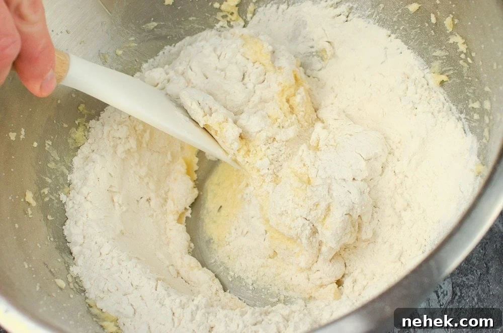 Perfect Lemon Drizzle Cake Recipe — Moist, Zesty Slice 18 Flour being added to the butter mixture in a silver bowl and being folded with a white and wooden spatula